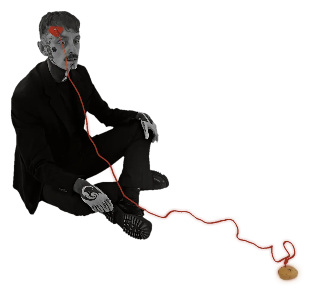 Simon sitting on the floor in a black suit, a red cable running from the patch on his forehead to a potato